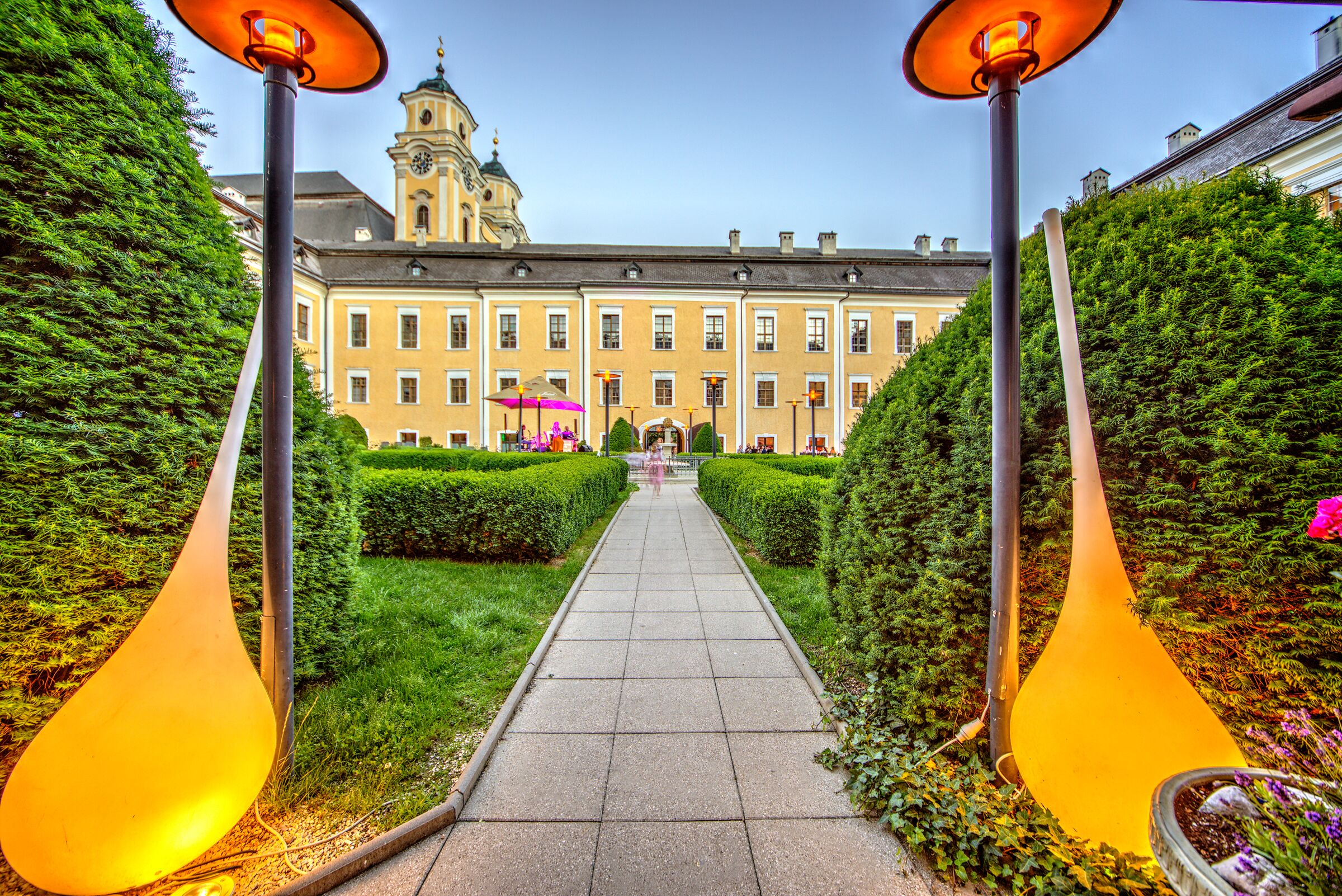 Am Eingang des Schlossgartens befinden sich links und rechts des Steinwegs Lampen und Büsche.